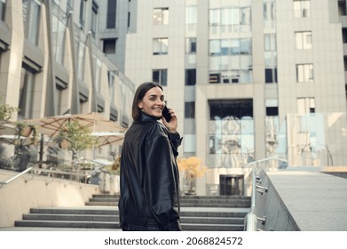 Cheerful young attractive brunette woman talking on mobile phone smiling toothy smile looking over shoulder at camera climbing stairs to modern office corporate high-rise building. - Powered by Shutterstock