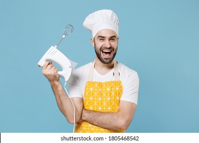 Cheerful young bearded male chef or cook baker man in apron white t-shirt toque chefs hat isolated on blue background studio portrait. Cooking food concept. Mock up copy space. Hold kitchen mixer