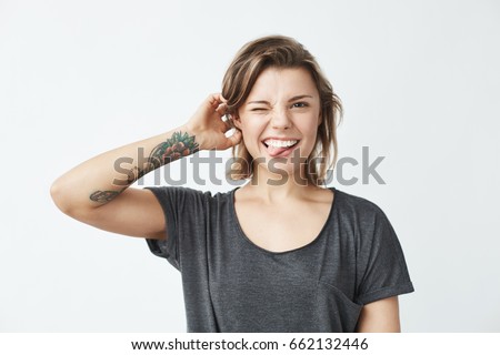 Cheerful young beautiful girl smiling winking showing tongue looking at camera over white background.