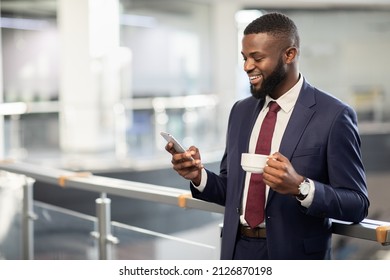Cheerful young black bearded man manager standing at office building corridor, drinking coffee, using mobile phone, chatting with business partner and smiling, panorama with copy space - Powered by Shutterstock