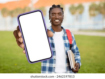 A cheerful young black man with braided hair carrying a red backpack, holds out a smartphone with a blank screen while standing on a university campus with buildings in the background - Powered by Shutterstock