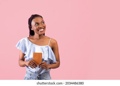 Cheerful Young Black Woman With Passport And Plane Tickets Looking Aside At Free Space, Going On Vacation, Traveling Abroad, Enjoying Overseas Trip Over Pink Studio Background