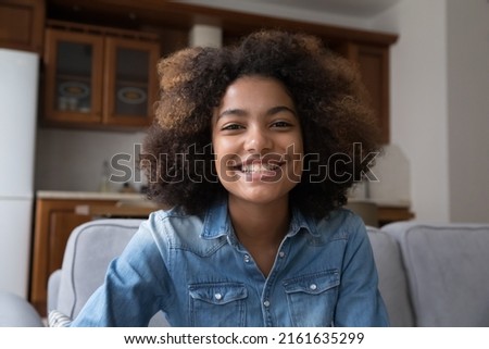 Cheerful young Black woman video blogger sitting on couch streaming live looking at web camera broadcasting on web channel recording clip. Webcam selfie portrait smiling teen female making video call