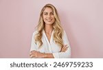 Cheerful young blonde woman standing confidently with arms crossed, expressing joy and happiness over a pink isolated background!