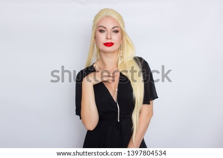 Cheerful young blonde woman wearing black evening dress standing isolated over white background, bright makeup