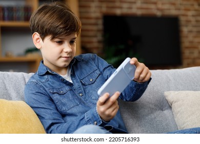 Cheerful young boy playing video game on smartphone sitting on sofa at home. Cute teenager playing in car racing game on mobile phone. Spending time at home, leisure, relax, happy carefree childhood - Powered by Shutterstock