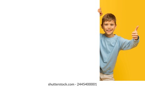 Cheerful young boy with a thumbs up sign, half behind a yellow background with space for text mockup - Powered by Shutterstock