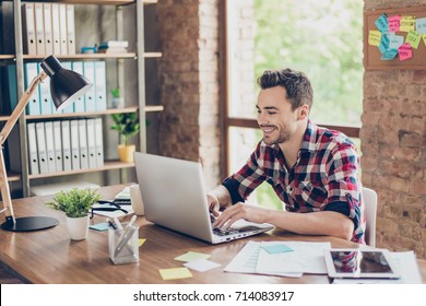 Cheerful Young Brunet Freelancer Is Smiling, Typing On His Laptop In Nice Modern Work Station At Home, In Casual Smart Wear