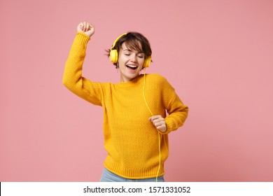 Cheerful young brunette woman girl in yellow sweater posing isolated on pastel pink wall background studio portait. People lifestyle concept. Mock up copy space. Listen music with headphones, dancing - Shutterstock ID 1571331052