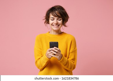 Cheerful Young Brunette Woman Girl In Yellow Sweater Posing Isolated On Pastel Pink Wall Background Studio Portait. People Lifestyle Concept. Mock Up Copy Space. Using Mobile Phone Typing Sms Message