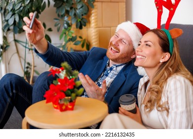 Cheerful young business people having fun celebrating Christmas at the office, wearing Santa hat and costume reindeer antlers having video call using smart phone - Powered by Shutterstock