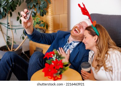 Cheerful young business people having fun celebrating Christmas at the office, wearing Santa hat and costume reindeer antlers having video call using smart phone and laughing - Powered by Shutterstock