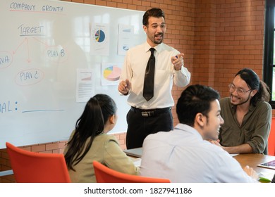 Alegre joven empresario caucásico con camisa de corbata hablando con alguien de su equipo durante la reunión con un ambiente relajado en la sala de reuniones de la oficina.