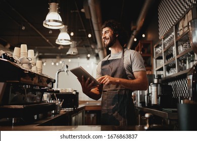 Cheerful young caucasian cafe owner wearing apron using digital tablet - Powered by Shutterstock