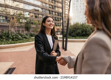 Cheerful Young Caucasian Female Director Shaking Hands With Job Seeker Spending Time Outdoors. Brunette Wears Black Jacket To Interview. Management Concept 