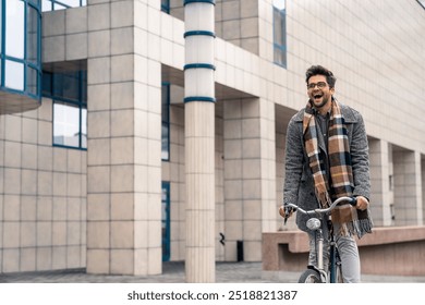 A cheerful young Caucasian man in smart casual attire rides his bicycle with enthusiasm, indicating a positive start to his workday in an urban setting. - Powered by Shutterstock