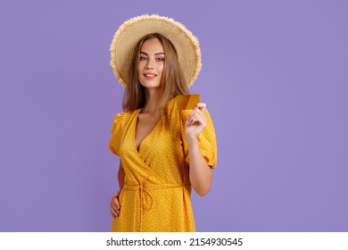 Cheerful young Caucasian woman in yellow dress and straw hat holding bank card isolated on purple background. - Powered by Shutterstock