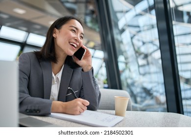 Cheerful Young Chinese Business Woman Talking On Phone Working In Modern Office. Happy Positive Asian Businesswoman Company Manager Wearing Suit Making Call On Cellphone Sitting At Workplace.