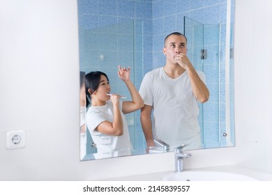 Cheerful Young Couple Brushing Their Teeth While Dancing Together In Front Of A Mirror In Bathroom. Shot At Home