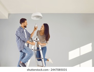 Cheerful young couple changing light bulb in apartment. Happy husband and wife standing on stairway in living room. Family couple moving in new house or doing renovations - Powered by Shutterstock