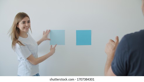 Cheerful Young Couple Choosing Wall Paint Color For Their New Home Decoration
