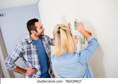 Cheerful Young Couple Choosing Wall Paint Color For Their New Home Decoration