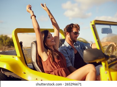 Cheerful young couple driving in a car. Enjoying road trip. Young man driving car with woman enjoying the ride with her hands raised.