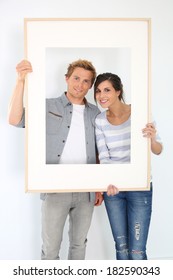 Cheerful Young Couple Holding Picture Frame To Look Through