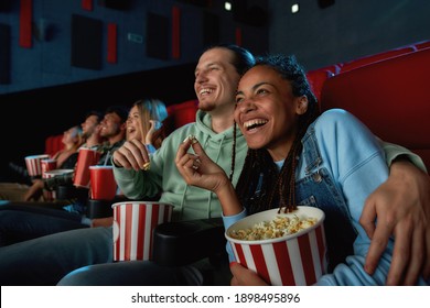 Cheerful young couple laughing, having popcorn, enjoying evening together while watching movie, sitting in cinema auditorium. Entertainment and people concept. Horizontal shot - Powered by Shutterstock