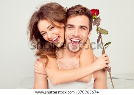 Cheerful young couple in love embracing in the bedroom with rose