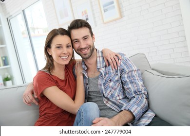 Fröhliches junges Ehepaar, das sich zu Hause auf dem Sofa entspannt