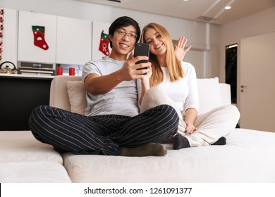 Cheerful young couple taking a selfie while sitting on a couch at home స్టాక్ ఫోటో