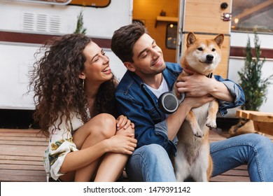 Cheerful young couple talking while standing at the campvan, petting a dog - Powered by Shutterstock