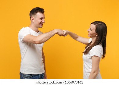 Cheerful young couple two friends guy girl in white empty blank design t-shirts posing isolated on yellow orange background in studio. People lifestyle concept. Mock up copy space. Giving fists bump - Powered by Shutterstock