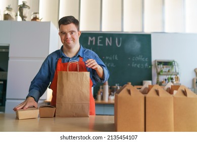 Cheerful young Down Syndrome waiter working in take away restaurant, social inclusion concept. - Shutterstock ID 2135454107