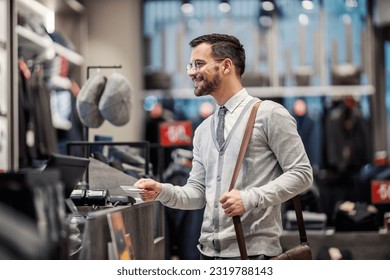A cheerful young elegant man is using his credit card on a pos device in a store.