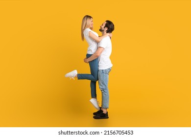 Cheerful young european male with beard raises female, isolated on yellow background, studio, full length, profile. Relationship, love, romance, advertising and offer, win and huge sale, copy space