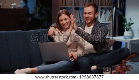 Cheerful young excited woman solving problem with internet connection rejoicing doing high-five with husband enjoying teamwork. Laptopcomputer. Home entertainment,