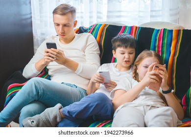 Cheerful Young Family Dad Son Teen Daughter Children Watching Online Video On Smartphone Sitting On Couch Together, Laughing Parent Kids Texting Playing Games Entertaining Using Mobile Phone Apps Home