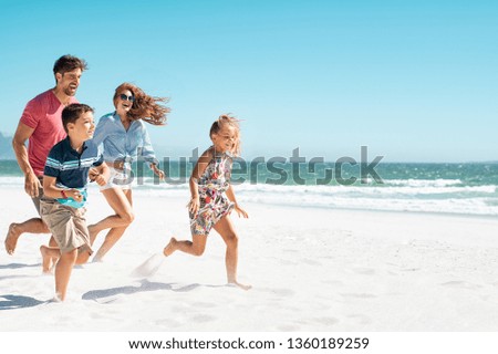 Cheerful young family running on the beach with copy space. Happy mother and smiling father with two children, son and daughter, having fun during summer holiday. Playful casual family enjoying.