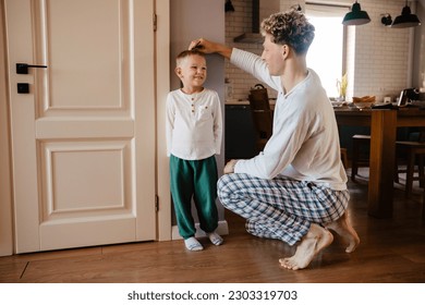 Cheerful young father measuring height of his cute son and marking it on wall at home - Powered by Shutterstock