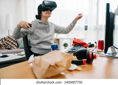 Cheerful Young Female College Student Exploring Virtual Reality Glasses Sitting In Messy Dirty Room At Table Of Trash Garbage Used Tissue. Happy Smiling Girl Geek In Vr Goggles Having Fun In Summer