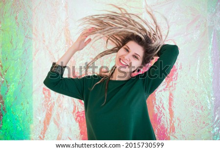 Cheerful young female in colorful outfit looking at camera with smile and shaking dreadlocks isolated on white background