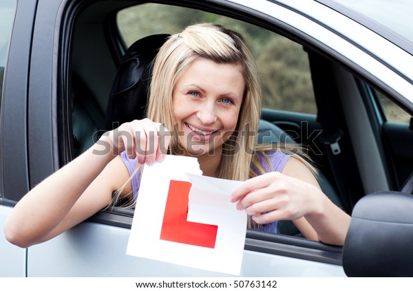Cheerful young female driver tearing up her L sign\
sitting in her car