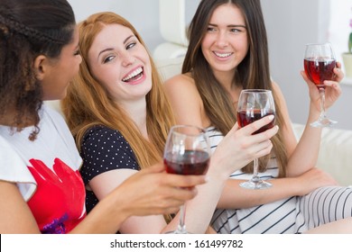 Cheerful Young Female Friends With Wine Glasses Enjoying A Conversation On Sofa At Home