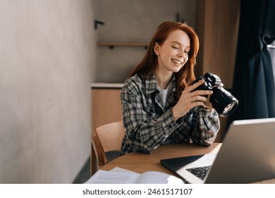 Cheerful young female photographer holding modern digital camera looking at screen choosing photos for editing while sitting in front of laptop computer at home office workplace in sunny day. - Powered by Shutterstock