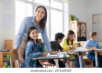 Cheerful young female teacher working in elementary school, happy teacher and girl smiling at camera in classroom interior - Powered by Shutterstock