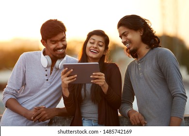 Cheerful young friends playing in digital tablet at outdoor background.