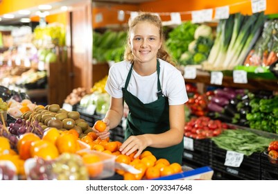 Cheerful young girl employees in uniform holding fresh mandarines in grocery shop - Shutterstock ID 2093347648