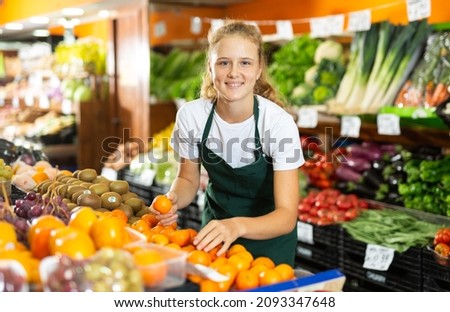 Cheerful young girl employees in uniform holding fresh mandarines in grocery shop